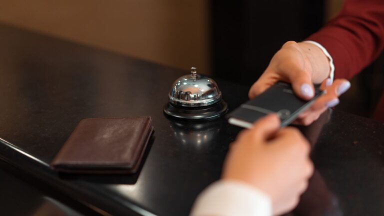 Guest handing a smartphone across a hotel reception desk while checking in with a mobile check-in app