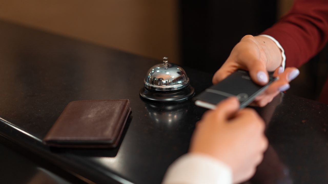 Guest handing a smartphone across a hotel reception desk while checking in with a mobile check-in app