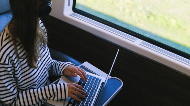 Passenger using a laptop on a European train, where train WiFi speeds average 7.6 Mbps